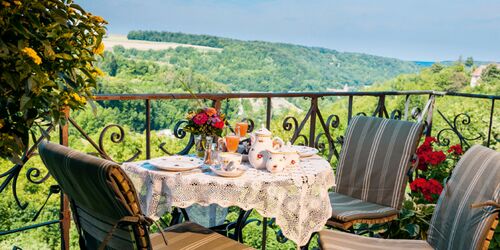 Gedeckter Balkontisch und Stühle auf einem Balkon vor einem grün bewachsenen Panorama