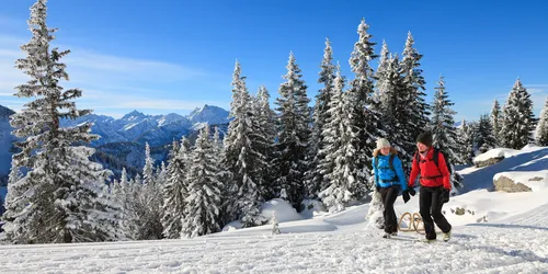 Wanderer mit Schlitten im Schnee vor Bergpanorama