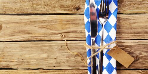 Holztisch mit Serviette im Muster der bayerischen Flagge sowie Messer und Gabel