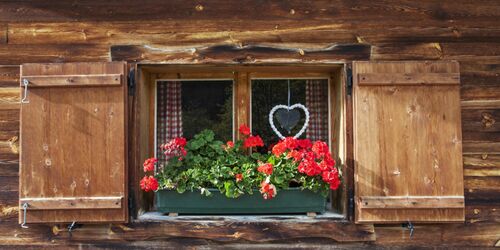 Hölzernes Fenster einer Hütte mit roten Blumen in Blumenkasten